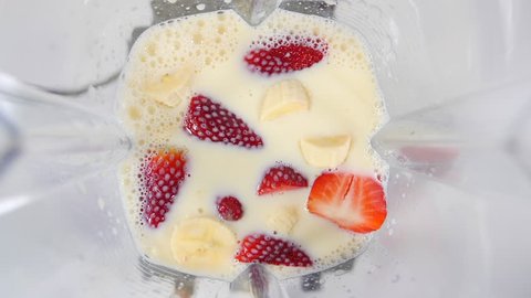 Smoothie blended in slow motion shot from above using fruit strawberries, bananas and yoghurt against a white background. Camera birds eye view. 