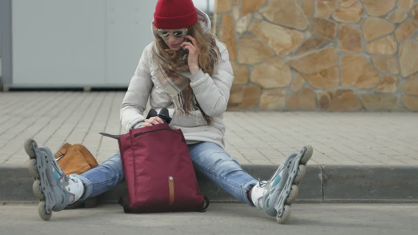 Young beautiful woman in red hat wearing sporty warm clothes and rollers, sitting on the asphalt road and taking pictures on a vintage camera 4k