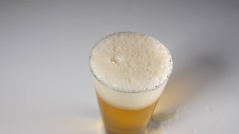 A beer being poured into a glass in slow motion , dolly shot against white background. Bartender pouring pint of alcohol at pub or bar