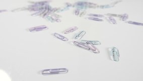 slow motion of pastel coloured paper clips fastener bouncing and falling onto a white surface,