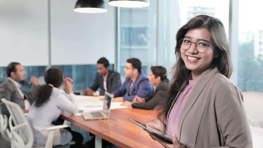 A happy and cheerful female office worker smiling in front of her team members. A cute woman employee or associate smiling while a group of executives interacting in the start up office boardroom
