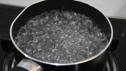 Boiling water with a furious buble and vapor in a dented pot, preparing for soup.