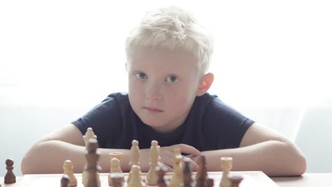 the boy albino plays chess, thinks over the move and makes a course on a sunny afternoon at the table