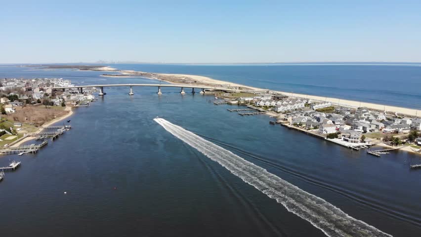Aerial video of the Intercoastal Waterway near Sandy Hook, New Jersey on the Shore and the Atlantic Ocean on a calm Spring day.  Shows the Intercoastal Waterway, boats, and houses.  New York City is v