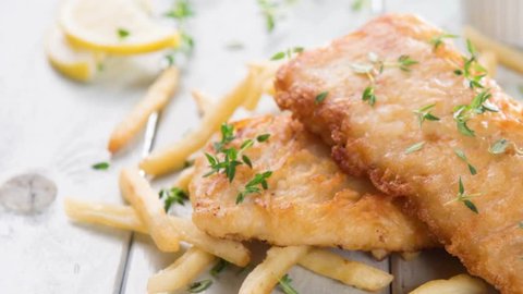 Fish and chips. Fried fish fillet with French fries on bright wooden background. 4k footage side panning.