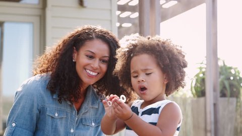 Young mixed race mother and daughter blowing bubbles outside Video Stok