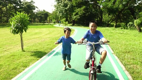 Little boy running follow his brother ride a bicycle in a park. स्टॉक व्हिडिओ
