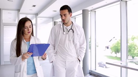 Young Medical Colleagues Analysing Paperboard While Walking Through Hospital : film stockowy