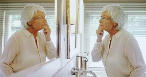 Senior caucasian woman looking at herself in mirror at home 4k
