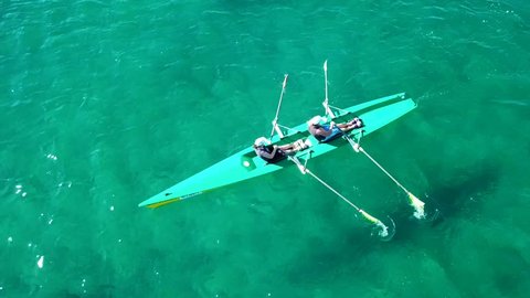 Aerial drone bird's eye view video of sport canoe operated by 2 young women in emerald tropical clear waters