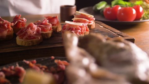 The work of a professional chef for the preparation of traditional Spanish tapas. Unfolding cheese plates on a layer of tomato and bacon.