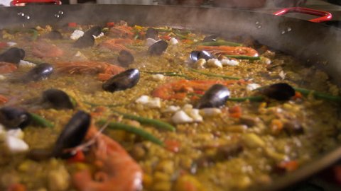 Preparation of Spanish paella. Adding olive oil to a mixture of rice, vegetables and seafood.