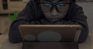 Close up of cute asian boy wearing eye glasses and using tablet computer ,Young teenage boy playing games on digital tablet .