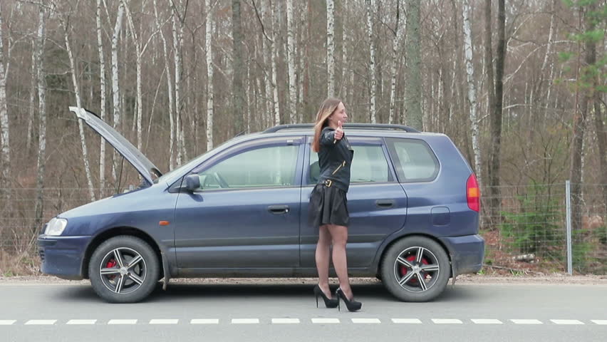 Young brown-haired woman stops for a ride near the broken machine. Handheld shot