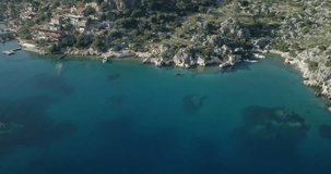 Aerial drone footage over Mediterranean Sea Turquoise Coast flyover Kalekoy village houses, necropolis, panning left reveal Simena Castle ruins near Ucagiz, Turkey. 4k at 23.97fps