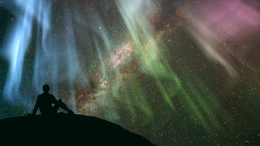The man sitting against the star shower with a northern light. time lapse