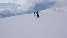 Two beginner skiers uncertainly and slowly descend one after another on a steep slope in the mountains at the ski resort. Slow motion, 4k, 3840x2160.