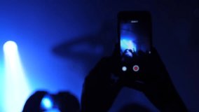 Mobile smart phone shooting a music concert by spectator silhouette hands in a stage lights