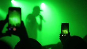 Mobile smart phone shooting a music concert by spectator silhouette hands in a stage lights