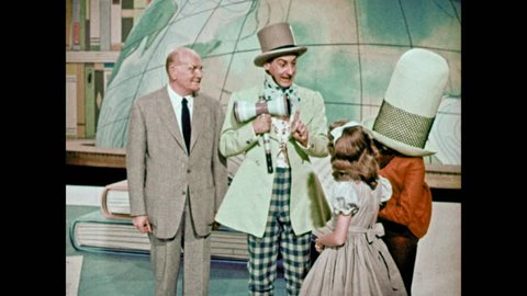1950s: Mad Hatter holds little girls hand and walks with her, Jabberwocky and man in suit. Jabberwocky claps and little girl takes notes.