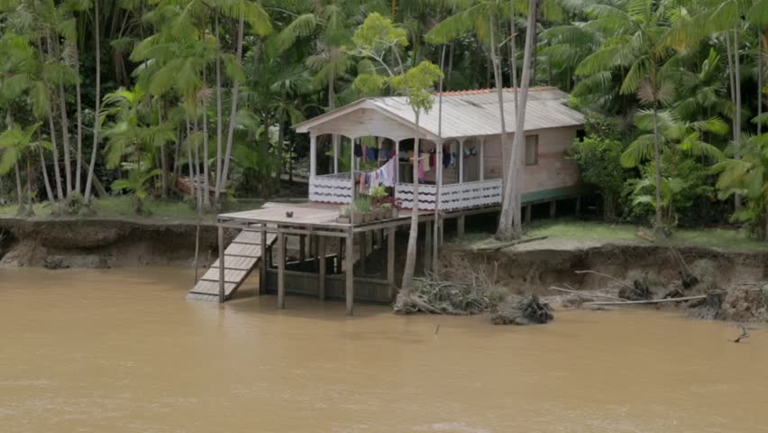 Moving shot of pretty white wooden stilt house with ramp and clothes drying on the banks of the Amazon River in Brazil