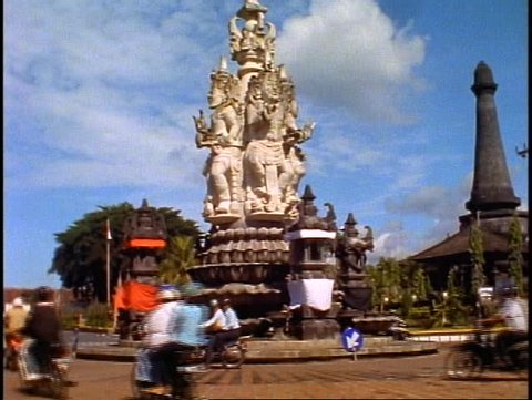 BALI, 1998, large statue of Hindu gods, traffic passes, tilt up medium shot