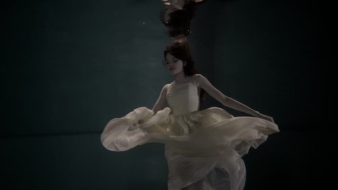 a young and pretty woman who looks like an actress swims at the bottom of the pool in a gorgeous dress, the lady participates in the art performance, she climbs to the top behind a breath of air