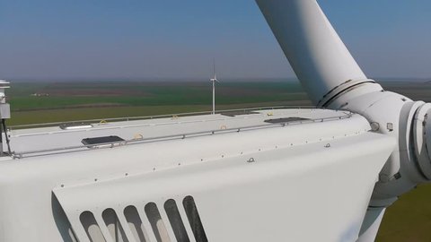 Aerial view of a rotating wind generator in a green field during the day. Electricity generation. The drone flies by next to the turbine. The windmill is close-up. Modern technologies.