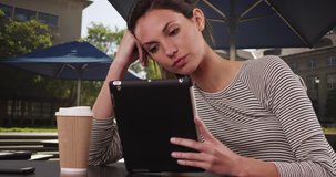 Millennial woman college student sitting at cafe table with tablet outside in university setting. Female in her 20s with coffee using pad device sitting outside on college campus. 4k