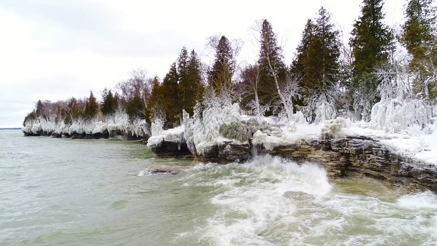 Scenic Rocky Wisconsin Wilderness shoreline with evergreen trees encased in thick ice. dreamlike slow motion view.