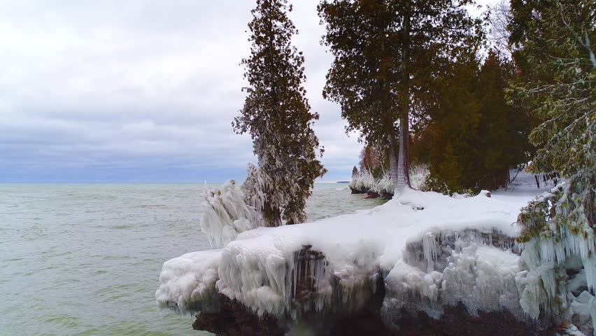 Scenic Rocky Wisconsin Wilderness shoreline with evergreen trees encased in thick ice. dreamlike slow motion view.