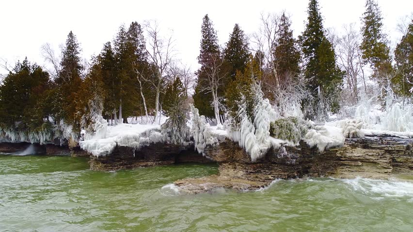 Scenic Rocky Wisconsin Wilderness shoreline with evergreen trees encased in thick ice. dreamlike slow motion view.