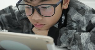 Close up of cute asian boy wearing eye glasses and using tablet computer ,Young teenage boy playing games on digital tablet .