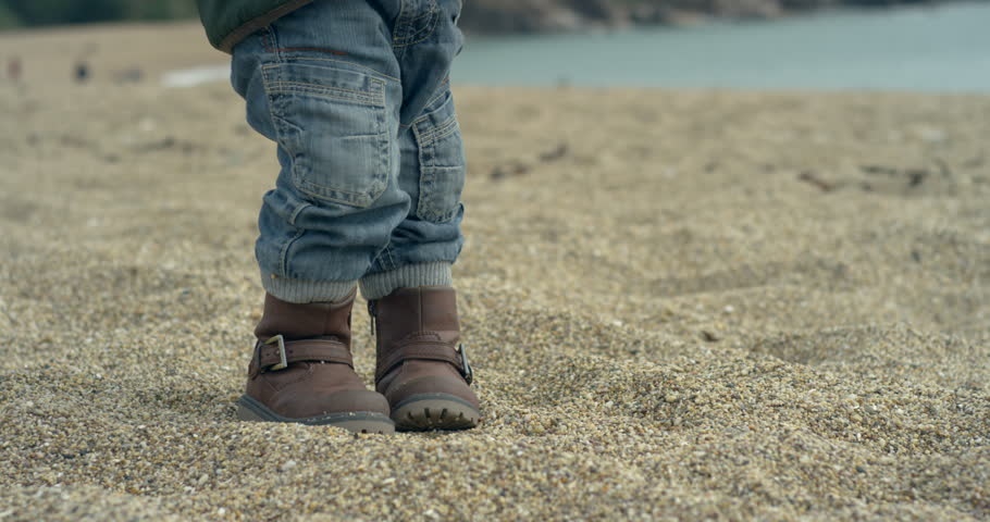 A little boy is walking on the beach in his boots. Slow motion handheld shot.