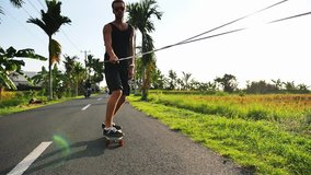 Skateboarder riding by the road near beautiful rice terraces, at Bali, Indonesian activity culture. Handsome man gonna to surf spot by skate. Surfing lifestyle adventure
