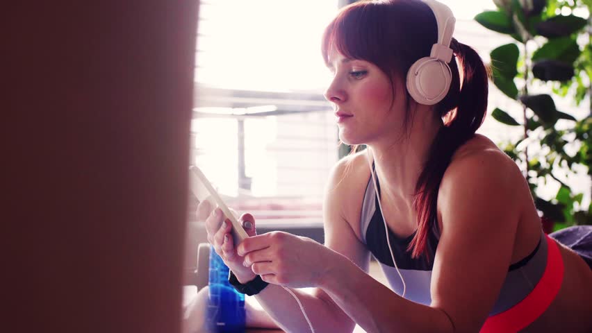 Young fitness woman with smartphone and headphones at home. | Shutterstock HD Video #1010253380