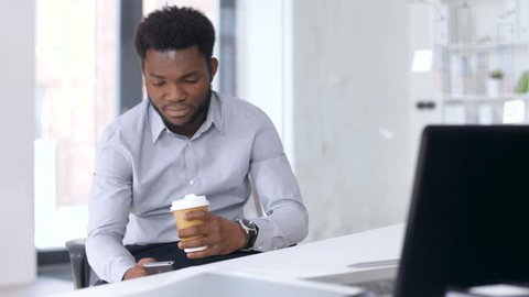 business, people and technology concept - african american businessman with smartphone having break and drinking coffee at office