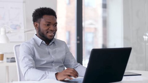 business, technology and communication concept - happy smiling african american businessman having video chat on laptop computer at office