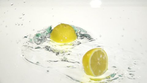 Two halves of lemon fall into the water. White background. Slow motion