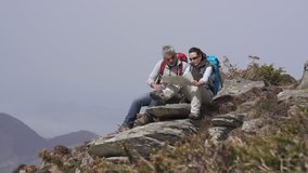 Couple of hikers reading orientation map sitted on rock