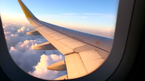 Airplane flight. Wing of an airplane flying above the clouds with sunset sky. View from the window of the plane. Airplane, Aircraft. Traveling by air. 4K UHD video