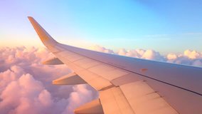 Airplane flight. Wing of an airplane flying above the clouds with sunset sky. View from the window of the plane. Aircraft. Traveling by air. 4K UHD video
