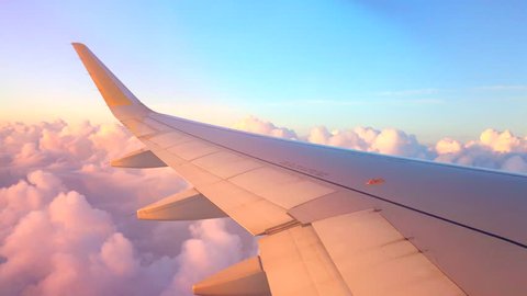 Airplane flight. Wing of an airplane flying above the clouds with sunset sky. View from the window of the plane. Aircraft. Traveling by air. 4K UHD video