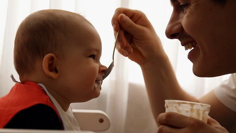 Slow motion of a young happy father feeds his son baby porridge.