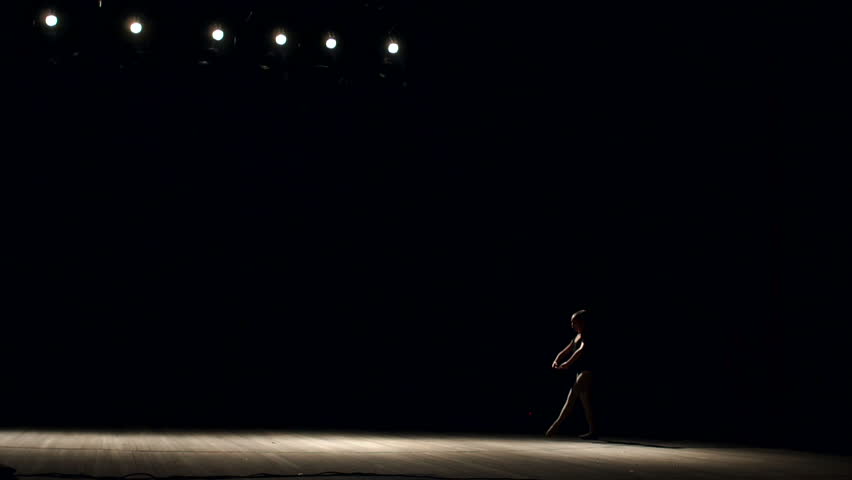 Girl ballerina doing horizontal twine in the air on stage on black background, slow motion. Girl doing gymnastic flip. Acrobatic flip. Ballet. Dancer.