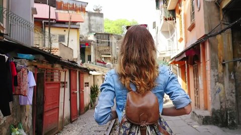 Back view. A young traveler woman walks the old city, by rail road and looks around. Vietnam, Hanoi city, Train street. Slow motion video