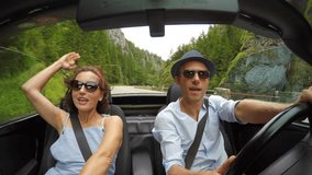 4K video: happy couple sings the songs while the roofless convertible car driving by the mountain road.