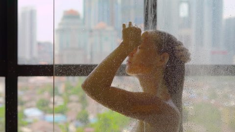 Young woman takes a shower in the bathroom with panoramic windows and silhouettes of skyscrapers outside the window