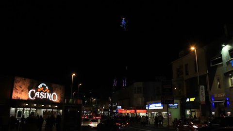 The lights on the Blackpool Tower changing colours in the background of black sky at night. City life - cars and people. England, October 2016