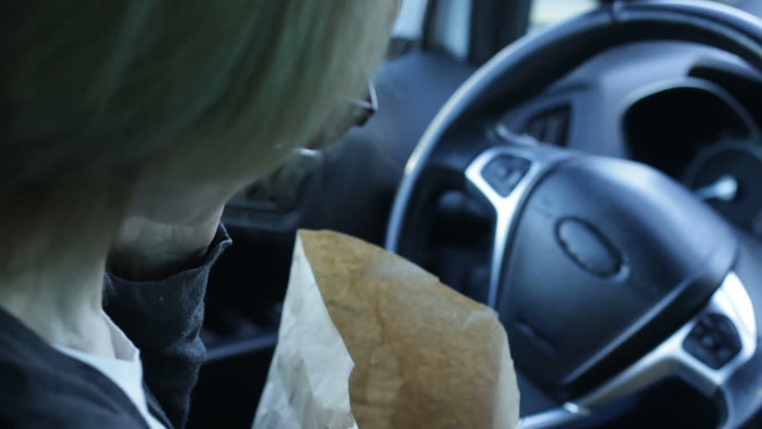 Adult lady sitting in car and eating fried potatoes and talking on phone